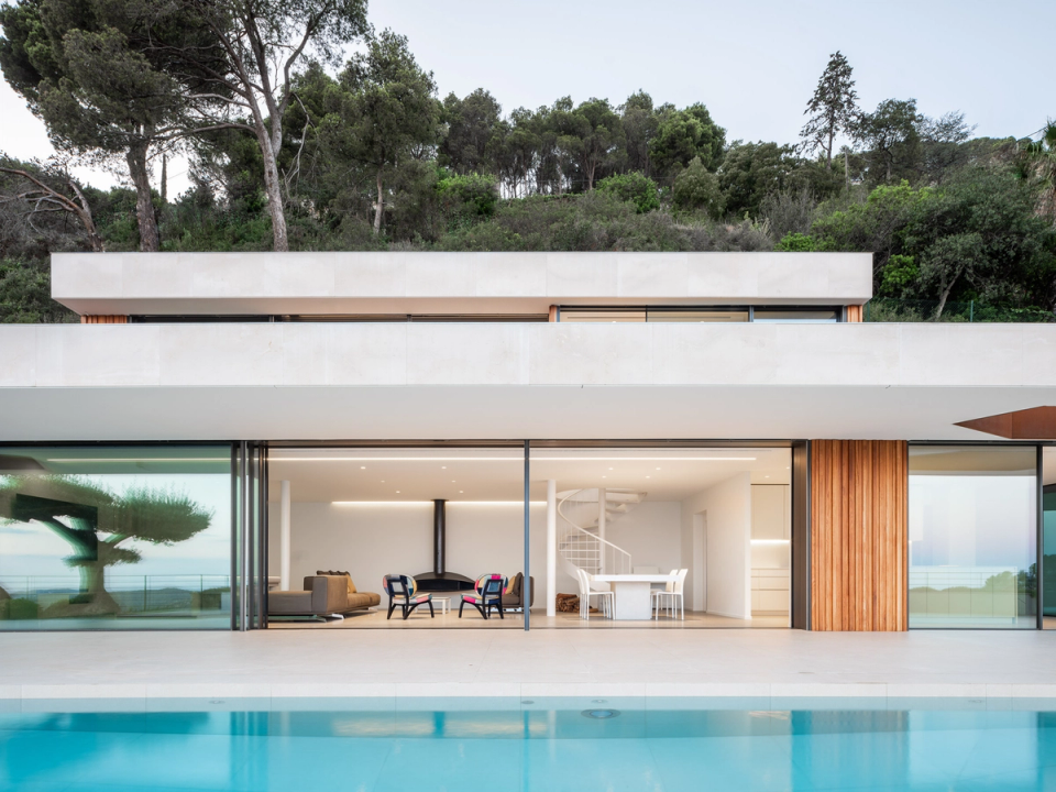 Modern detached single-family home with a minimalist façade, large glass surfaces, and open spaces directly connected to the pool and outdoor areas. The combination of concrete, natural wood, and neutral tones defines an elegant and functional architecture, while the interior renovation prioritizes natural light, visual openness, and continuity between interior and exterior spaces to create a sophisticated contemporary home.