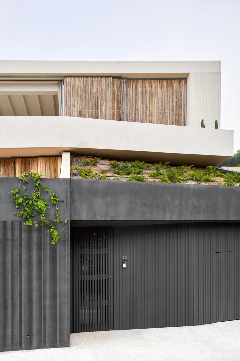 This single-family home combines contemporary architecture and landscape integration through a composition of clean lines and natural materials. The elevated volumetry follows the slope of the terrain and creates a light and horizontal image that strengthens the connection with the surroundings. The wood cladding adds texture and warmth to the façades, while the dark base walls create contrast and define the access and technical spaces of the home. The incorporation of vegetation on the roofs and embankments helps merge this single-family home with the Mediterranean landscape and promotes discreet, sustainable, and elegant architecture.