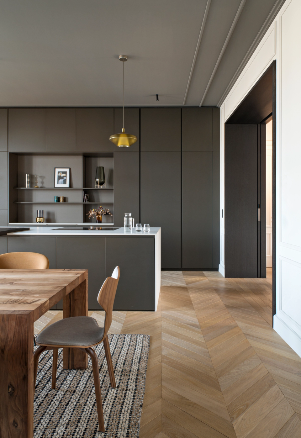 The interior renovation of this home combines contemporary elegance and original elements to create sophisticated and functional spaces. The open kitchen, featuring minimalist furniture and dark tones, contrasts with the warmth of the herringbone parquet flooring and natural wood, achieving a balanced, bright atmosphere designed to enhance everyday comfort.