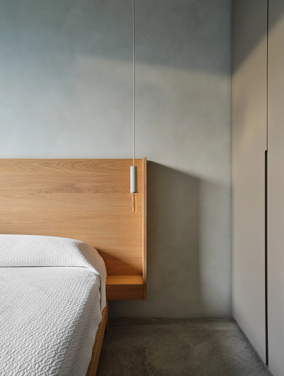 Housing renovation with a minimalist bedroom where material continuity brings order and serenity. The renovation combines natural wood, soft light and integrated details to create a warm, balanced and functional space.