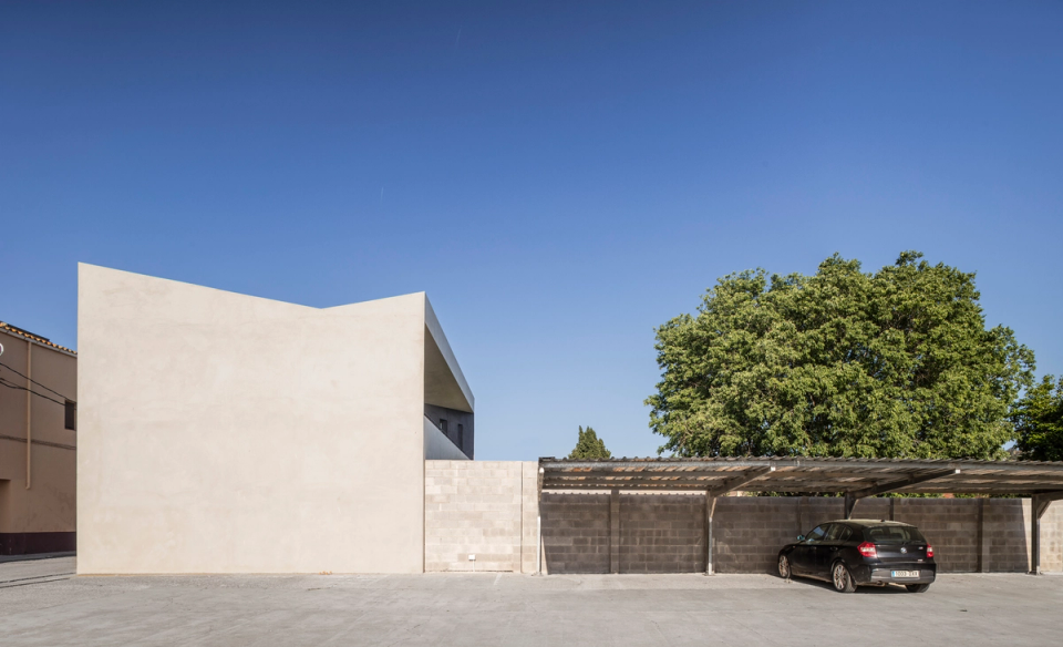 The volumetry of the house emerges above the perimeter walls with a clear and powerful geometry. The large overhang protects the upper façade and creates a contemporary and serene image, while neutral materials and surrounding vegetation reinforce the integration of the house within the residential environment.