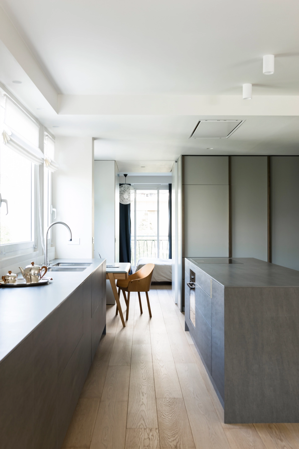 Minimalist interior renovation with a contemporary kitchen and central island, interior architecture featuring a natural wood-clad volume, open and functional space, modern black designer stools, light oak parquet flooring, refined and elegant lines, integrated handleless furniture, contemporary Nordic style, warm and bright atmosphere, high-end modern interior design with natural materials and neutral tones.