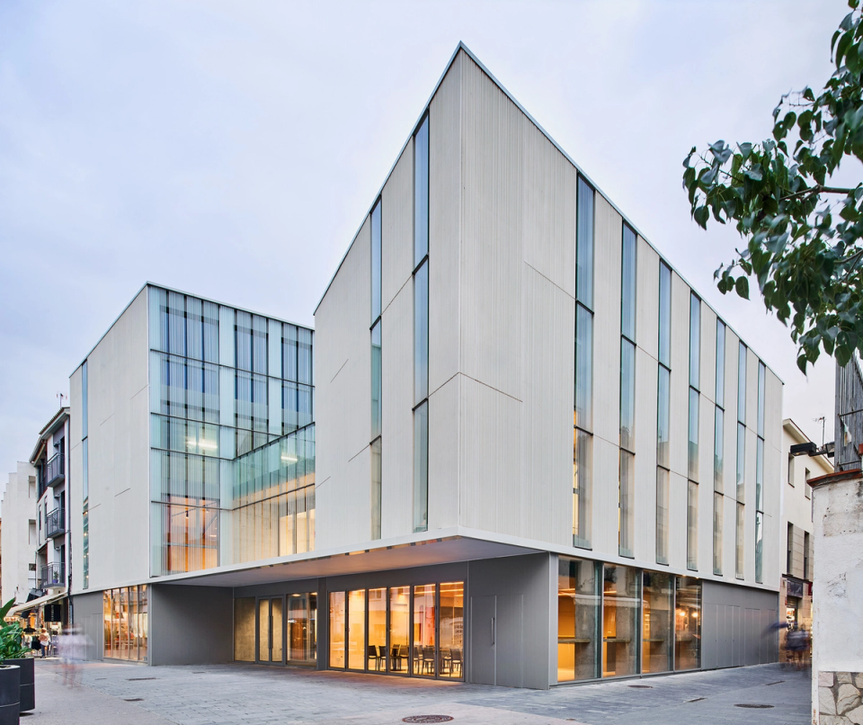 Minimalist façade of a cultural center conceived as a contemporary architectural piece integrated into the public space. Vertical lines, metallic finishes, and large glazed surfaces bring rhythm, transparency, and brightness to the building, reinforcing its institutional identity. The open ground floor connects the cultural center with the urban square, creating an accessible and welcoming space intended for cultural, educational, and social activities. A functional and elegant architecture that turns the facility into a new cultural and civic landmark.