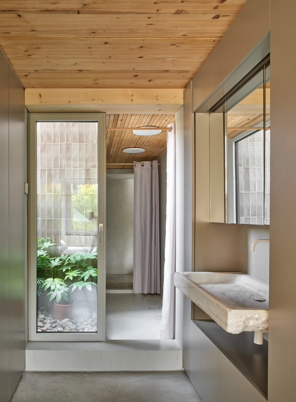 Housing renovation with a bathroom connected to a small inner courtyard that brings natural light and ventilation to wet areas. The renovation integrates continuous materials, wood and vegetation to create an intimate, functional and relaxing atmosphere.