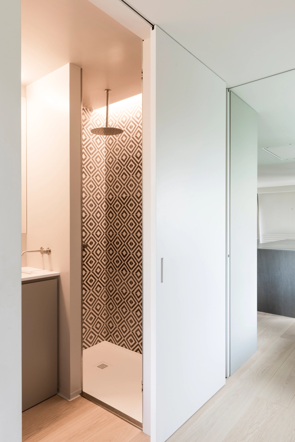 Interior renovation of a modern shower with glass enclosure, rain-effect showerhead, and geometric gray-toned wall cladding that brings personality, spaciousness, and a contemporary style to the bathroom.