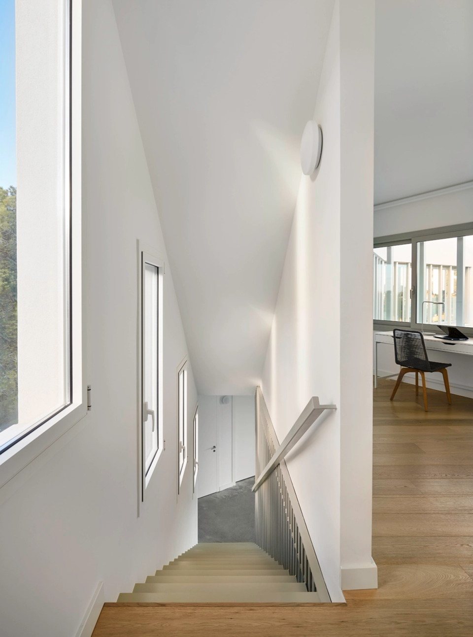 Interior of a detached single-family home with minimalist staircase, open spaces, and architecture defined by natural light. Light-toned finishes and natural wood provide spaciousness, warmth, and visual continuity throughout the residential project.