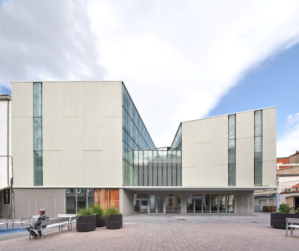 Front view of a contemporary cultural center designed to open itself to the urban space and become a civic meeting point. The building combines clean volumes, metallic façades, and large glass surfaces that enhance natural light and visual transparency between interior and exterior. The access square reinforces the public and accessible character of the cultural center, creating a welcoming environment for social, cultural, and educational activities. A modern and functional architecture that brings identity and dynamism to the urban core.