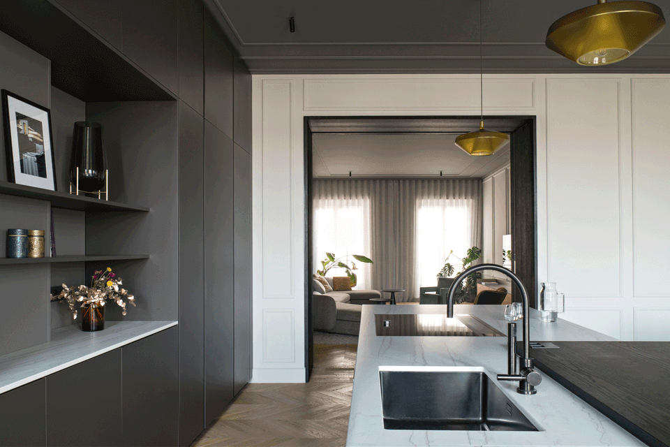 The interior renovation of this kitchen embraces a sophisticated and contemporary aesthetic that respects the original character of the home. The contrast between dark finishes, classical moldings, and light surfaces creates an elegant and balanced space, while the visual connection with the living room reinforces the feeling of spaciousness, brightness, and continuity between environments.