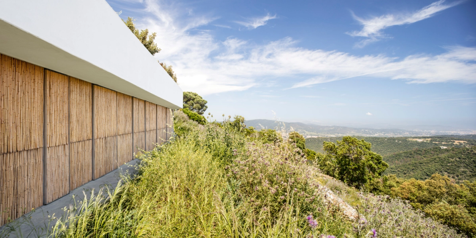 Detached house surrounded by native vegetation and naturally integrated into the slope of the terrain, featuring a façade clad with organic materials that reinforce the relationship between architecture and landscape. Open views and the Mediterranean surroundings create a sense of calm, privacy and connection with nature.