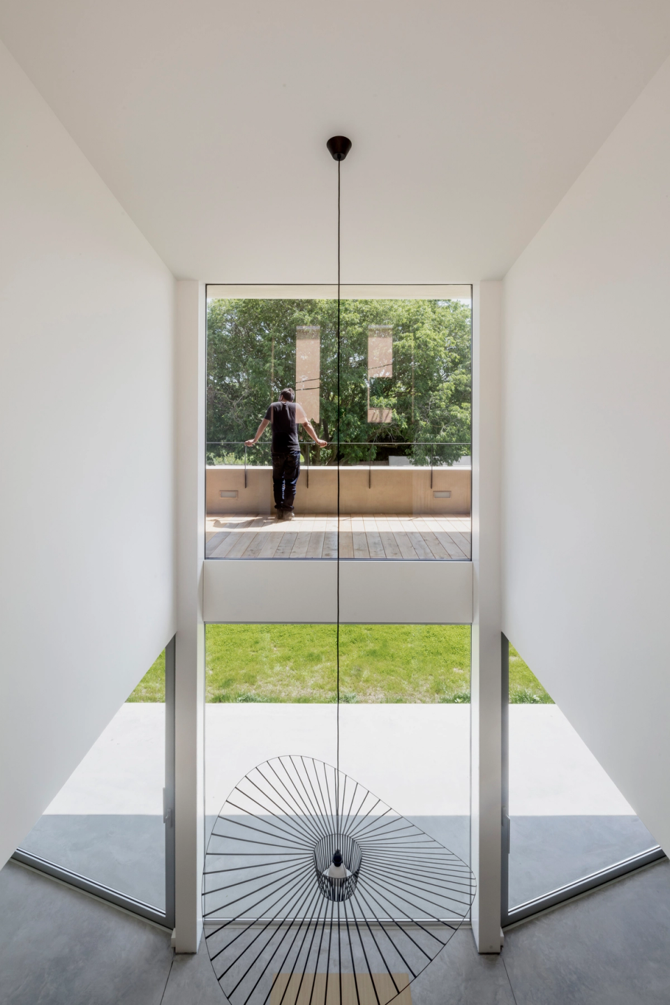 The double-height space becomes the central element of the interior, visually connecting the different floors and enhancing the entry of natural light. Large openings frame the garden views, reinforcing the sense of spaciousness, transparency, and continuity between interior and exterior.