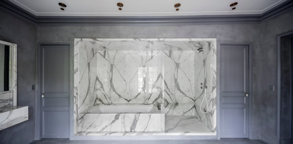 This interior renovation proposal stands out for its sophisticated and minimalist design, where large-format marble becomes the absolute protagonist of the bathroom space. The natural veining of the cladding creates an artistic and elegant composition that conveys exclusivity, while the integrated bathtub and clean lines reinforce a contemporary and refined aesthetic. The combination of gray tones, continuous surfaces, and high-quality finishes conveys spaciousness, brightness, and a timeless sense of luxury ideal for modern homes.
