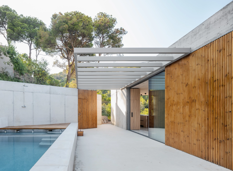 This single-family home in Begur stands out for its direct relationship with the landscape and Mediterranean light, integrating interior and exterior spaces into a single architectural experience. The combination of exposed concrete, natural wood, and large glazed surfaces provides a contemporary, elegant, and timeless aesthetic, while the pool area and outdoor pergola create an open, functional living space designed to enjoy the privileged surroundings of the Costa Brava.