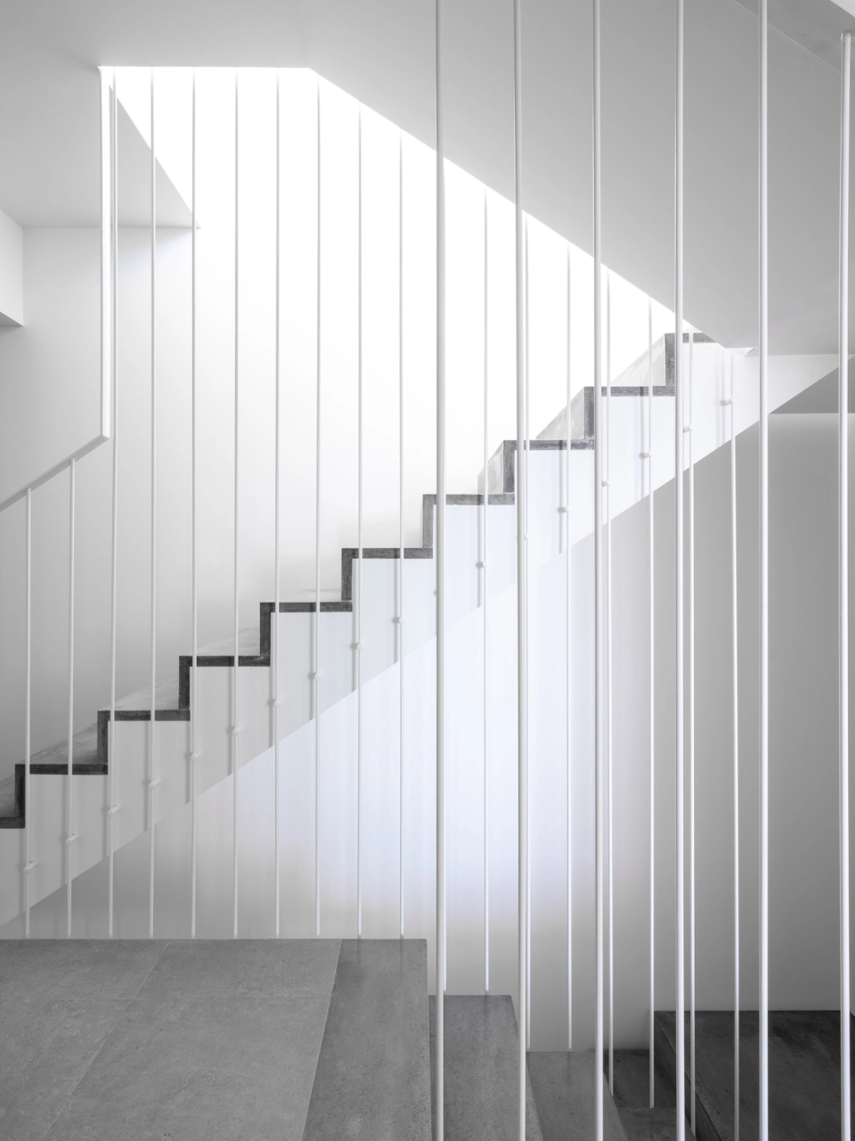 Interior space of a detached single-family home designed according to principles of formal purity, natural light, and spatial continuity. The straight staircase, integrated into a minimalist architecture with neutral tones, acts as the connecting axis between floors, while zenithal light reinforces the feeling of spaciousness and serenity. The combination of continuous flooring, clean lines, and an open layout creates a contemporary, functional, and elegant atmosphere designed to enhance comfort and the relationship between the different spaces of the house.
