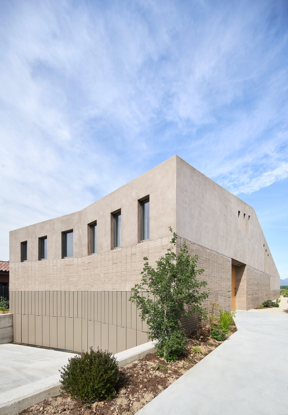 This single-family home features an architecture of soft and contemporary lines, with a façade combining mineral and ceramic textures to provide rhythm and personality. The integration of landscaping and natural materials reinforces the relationship between the house and the outdoor environment.