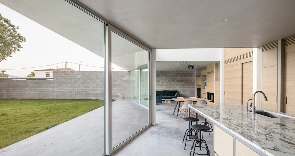 Interior of a detached single-family home with an open kitchen, large glass enclosures, and direct connection to the outdoor garden. The project embraces open-plan spaces, natural materials, and contemporary architecture designed to enhance natural light and everyday functionality.