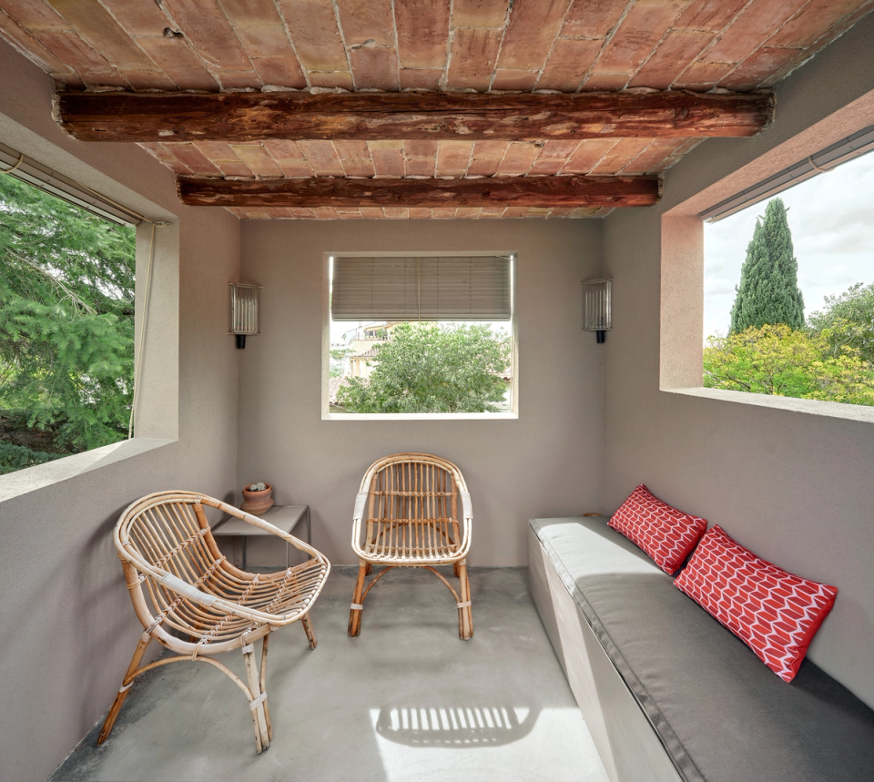 Housing renovation with an old gallery transformed into a small, bright and sheltered living room. The renovation restores original elements such as wooden beams and creates welcoming spaces connected to the outdoors.