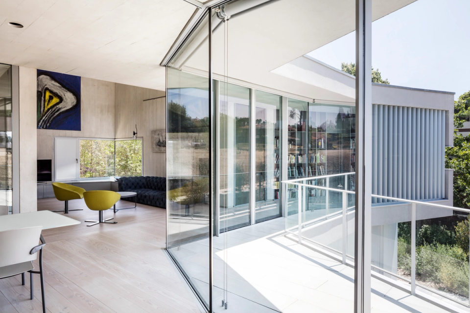 Interior of a contemporary single-family home with minimalist architecture, large open spaces, and generous ceiling heights that enhance the feeling of spaciousness. Exposed concrete finishes, neutral surfaces, and large glazed openings create a bright and sophisticated atmosphere, naturally connecting the interior spaces with the outdoors. Designer furniture and contemporary artworks bring contrast, color, and personality to this modern and elegant living room.