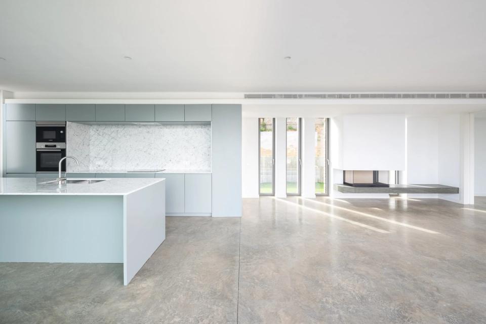 Detached single-family home with a contemporary kitchen open to the outdoors through large panoramic windows. Natural stone finishes and neutral tones provide elegance and brightness, reinforcing the visual connection with the terrace and landscape.