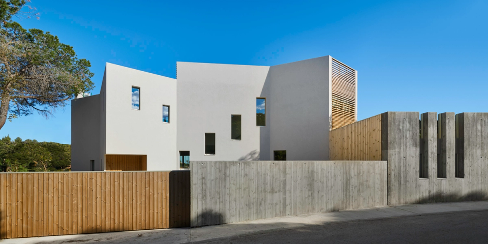Detached single-family home with contemporary architecture featuring pure geometric volumes and a minimalist composition that stands out for its balance between privacy, natural light, and integration with the surroundings. The combination of exposed concrete, wooden cladding, and large vertical openings brings warmth and character to a project designed to connect functionality and design.