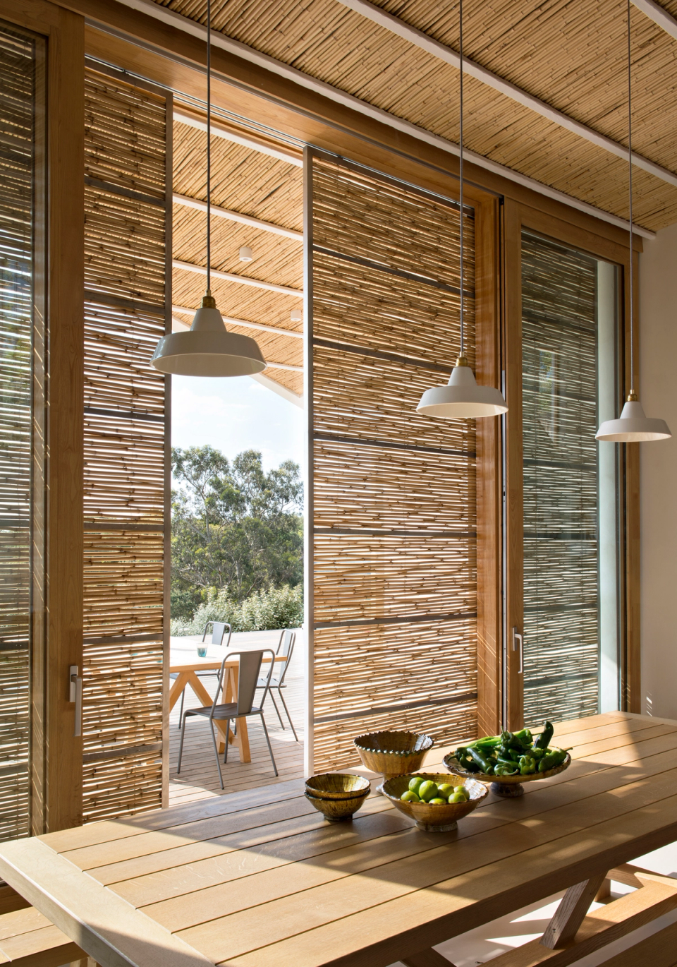 Interior of a detached house with large wooden enclosures and natural solar protections that filter Mediterranean light. The space stands out for the use of warm materials, ceilings clad with natural fibers and a fluid connection with the outdoor terrace, bringing comfort, brightness and integration with the surroundings.