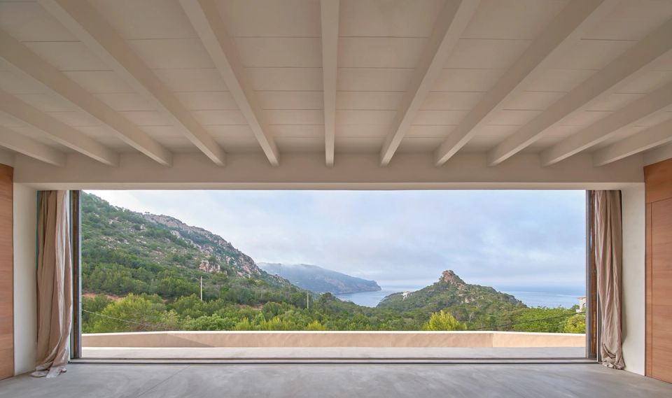 This single-family home prioritizes a direct relationship with the landscape through a large panoramic opening that frames views of the sea and the natural surroundings. The interior space, with clean lines and warm materials, is conceived as an extension of the exterior, enhancing the feeling of spaciousness, brightness, and calm. The exposed white wooden structure reinforces the Mediterranean character of the architecture, while the minimal presence of elements allows the landscape to become the true protagonist of the home. This single-family home combines contemporary design, integration with nature, and open spaces designed to enjoy the views and natural light throughout the day.
