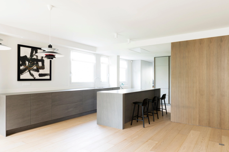 Interior renovation of an open kitchen with a contemporary central island, bright open-plan space, minimalist furniture in dark tones and natural wood, elegant and functional interior design, kitchen integrated into the living room, light oak parquet flooring, clean architectural lines, modern black stools, Scandinavian-style pendant lighting, high-end contemporary interior design, warm and sophisticated atmosphere with minimalist Nordic aesthetics.
