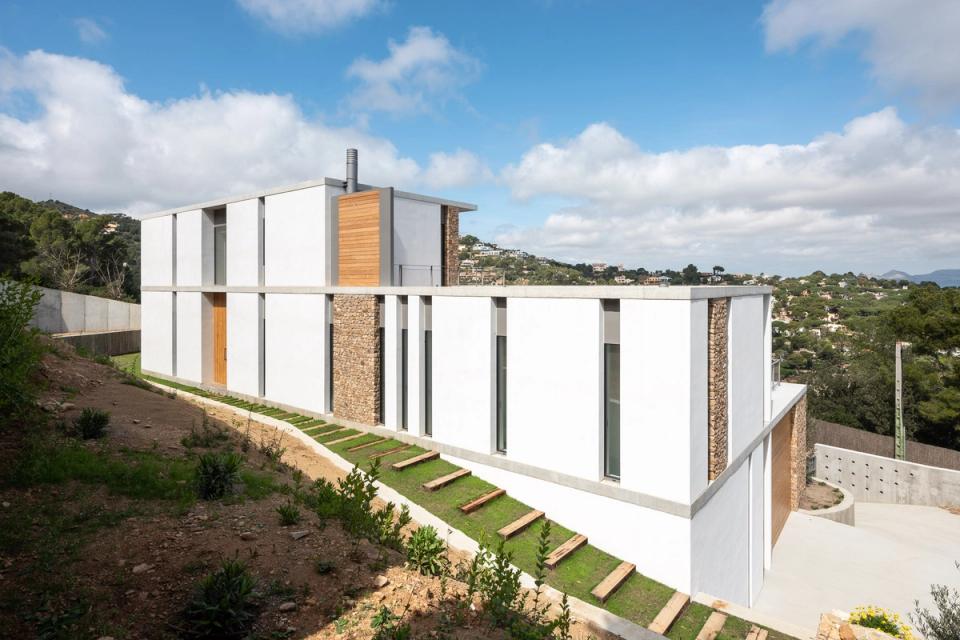Detached single-family home with a modern façade defined by the combination of natural stone, concrete, and white minimalist volumes. Vertical openings provide rhythm, natural light, and a subtle connection between interior and exterior spaces.