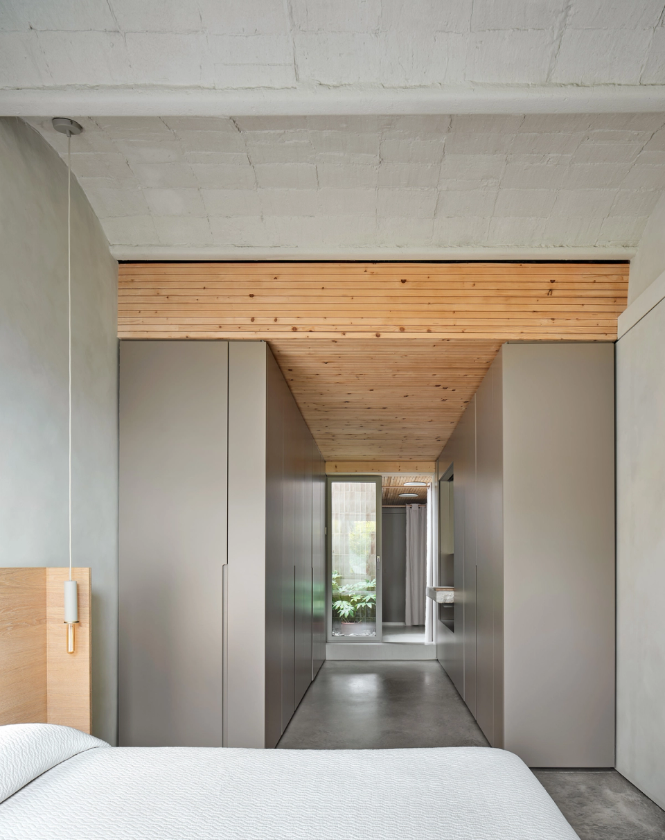 Housing renovation with a functional layout connecting bedroom, dressing room and bathroom through a fluid and orderly circulation. The renovation combines visual continuity, natural materials and wooden ceilings to enhance spaciousness and comfort.