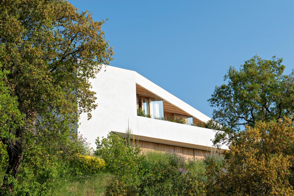Detached house integrated into the natural landscape through minimalist architecture with clean lines and organic materials. The home adapts to the topography and Mediterranean vegetation, combining white façades, wood and large openings to enhance natural light and the connection with the surroundings.