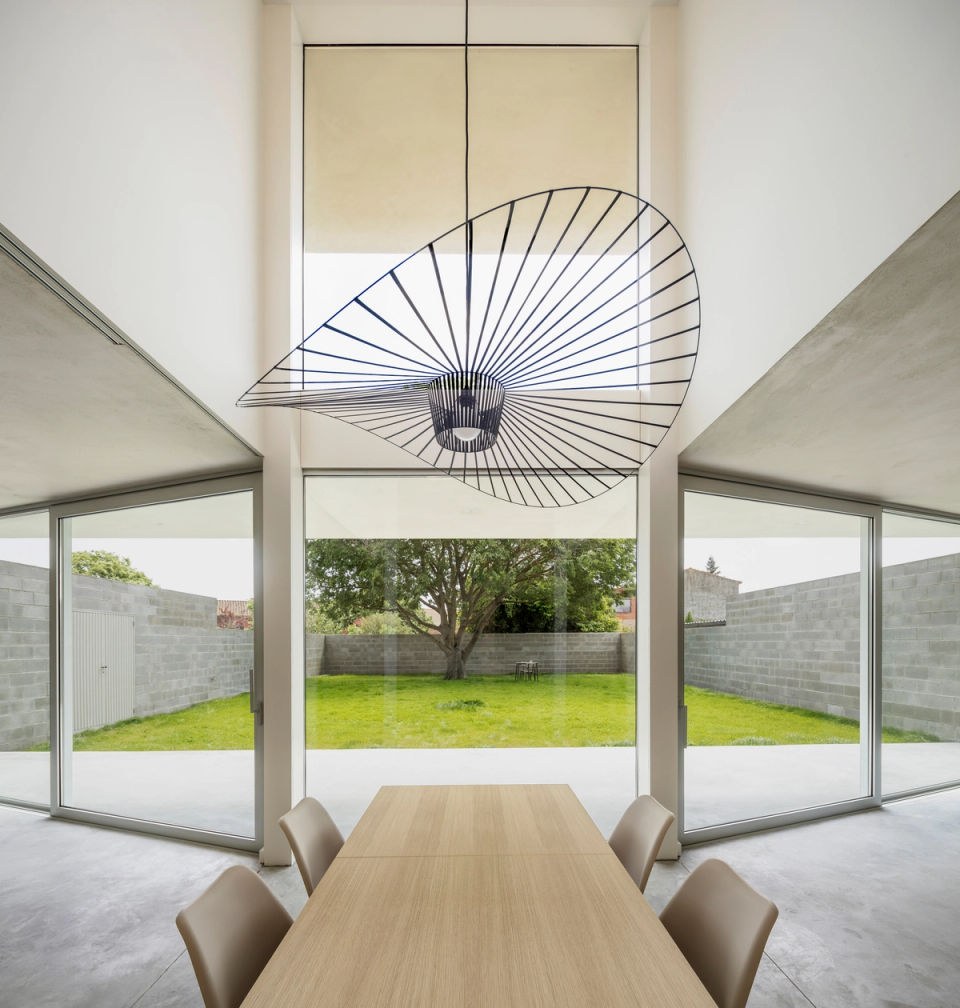 Contemporary detached single-family home with pure lines and strong volumetry, organized around a large central garden that acts as the visual and spatial core of the house. The project contrasts a fully open and transparent ground floor, defined by large sliding glass enclosures, with a more solid and introspective upper volume that appears to float above the lower level.