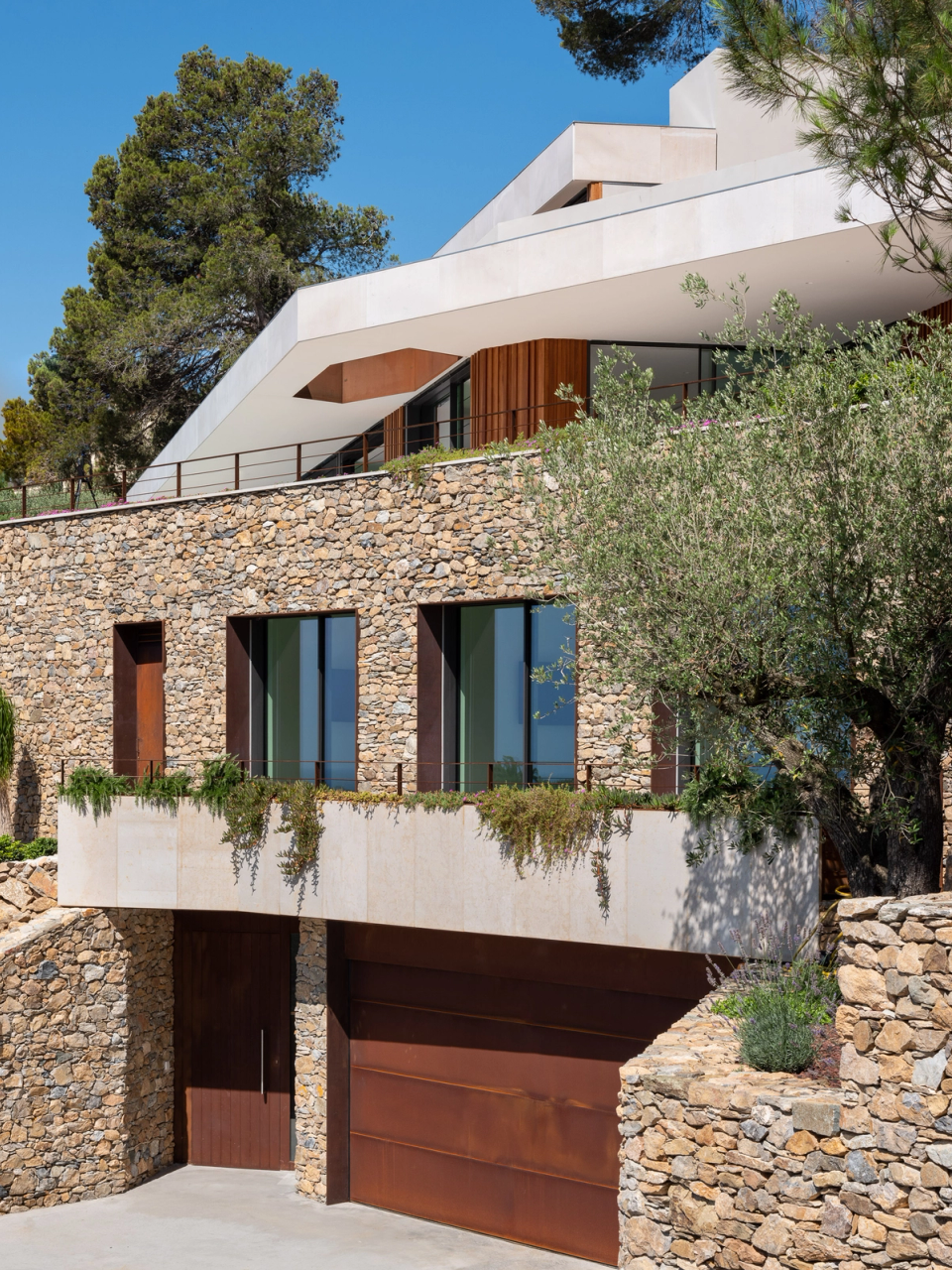 Detached single-family home with contemporary architecture integrated into the Mediterranean landscape, where natural stone, concrete, and wood create an elegant and timeless composition. The stepped volumetry adapts to the slope of the site and enhances views and natural light in all interior spaces. This interior renovation stands out for the balance between noble materials, pure lines, and a fluid connection between interior and exterior, creating a sophisticated, functional home fully integrated with its surroundings.