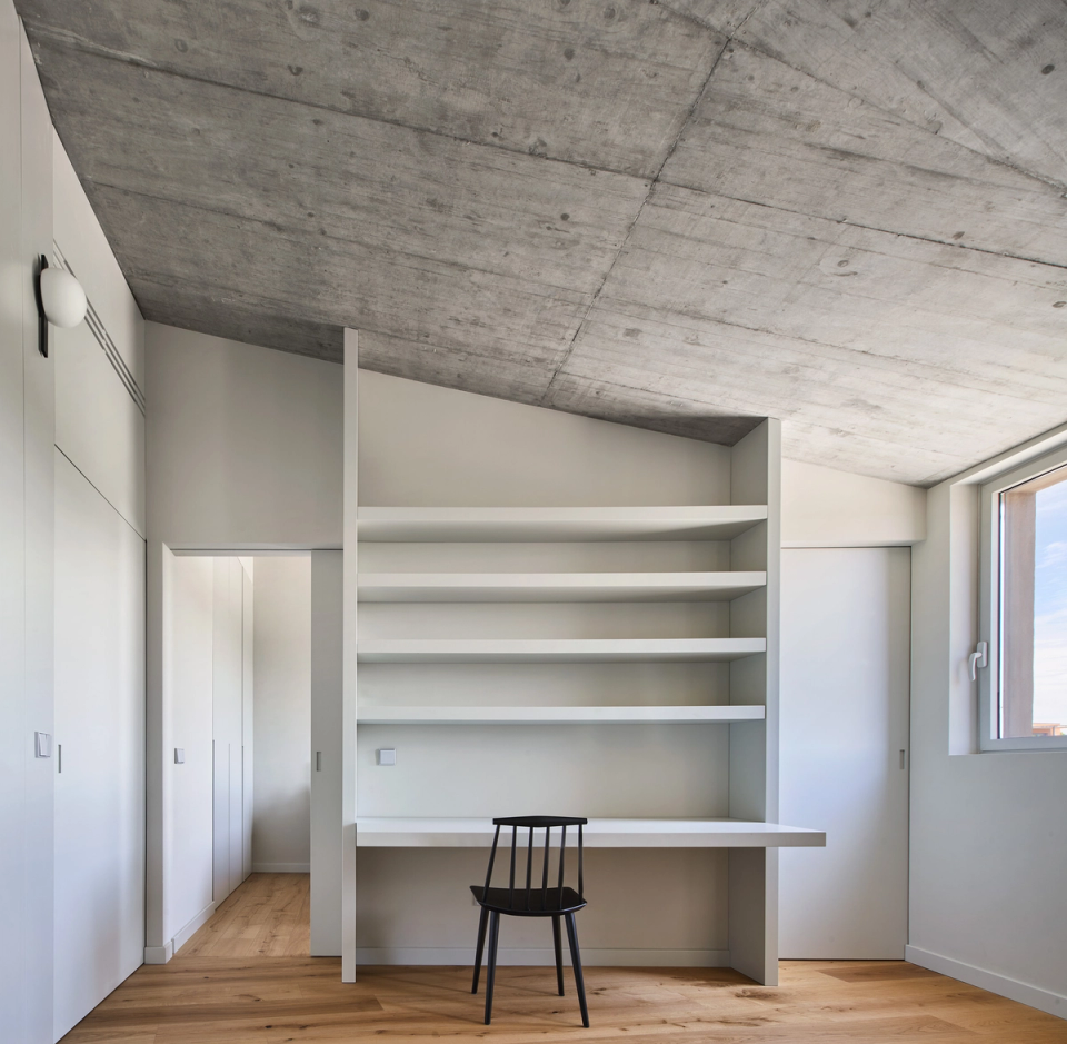 This study within the single-family home combines functionality and minimalism with a clean and bright interior design proposal. Integrated shelving, the exposed concrete ceiling, and natural wood finishes create a serene atmosphere designed to encourage concentration and everyday comfort.