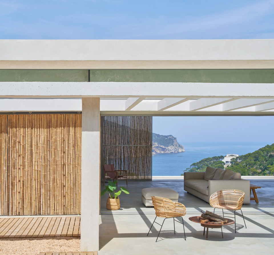 This single-family home opens completely to the Mediterranean landscape through large covered outdoor spaces and architecture designed to enhance sea views. The structural pergola filters natural light and creates comfortable shaded areas that connect the living room fluidly with the exterior. Natural wood cladding and vegetal textures reinforce the integration of the home with its surroundings, bringing warmth and naturalness to the spaces. This single-family home combines contemporary design, spaciousness, and a constant relationship with the landscape to create elegant, open architecture focused on well-being.