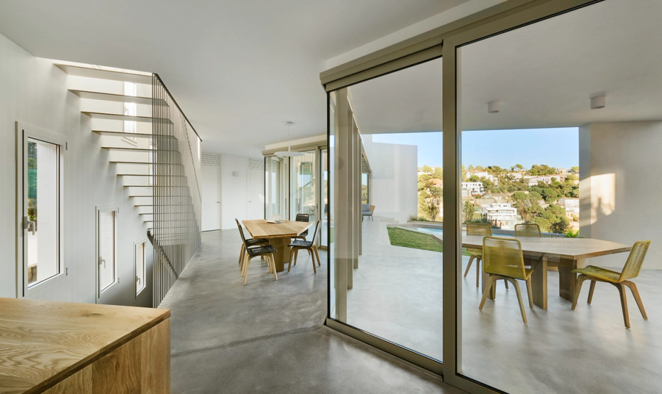 Detached single-family home with minimalist interiors and refined architecture distinguished by natural light and simplicity of materials. The lightweight metal staircase and wooden door provide contrast and warmth to a contemporary space designed to enhance visual spaciousness and functionality.