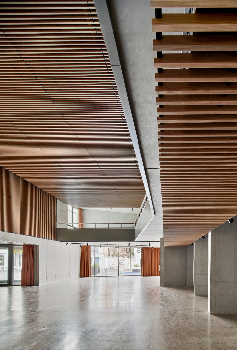 Interior space of a cultural center conceived with an open, flexible, and bright architecture designed to host cultural activities, exhibitions, and public events. The large central lobby stands out for its ceilings clad with wooden slats, exposed concrete finishes, and open-plan layout that enhances visual spaciousness and circulation between floors. The combination of warm and industrial materials gives the cultural center a contemporary identity, creating a functional, welcoming, and adaptable environment for multiple civic uses.