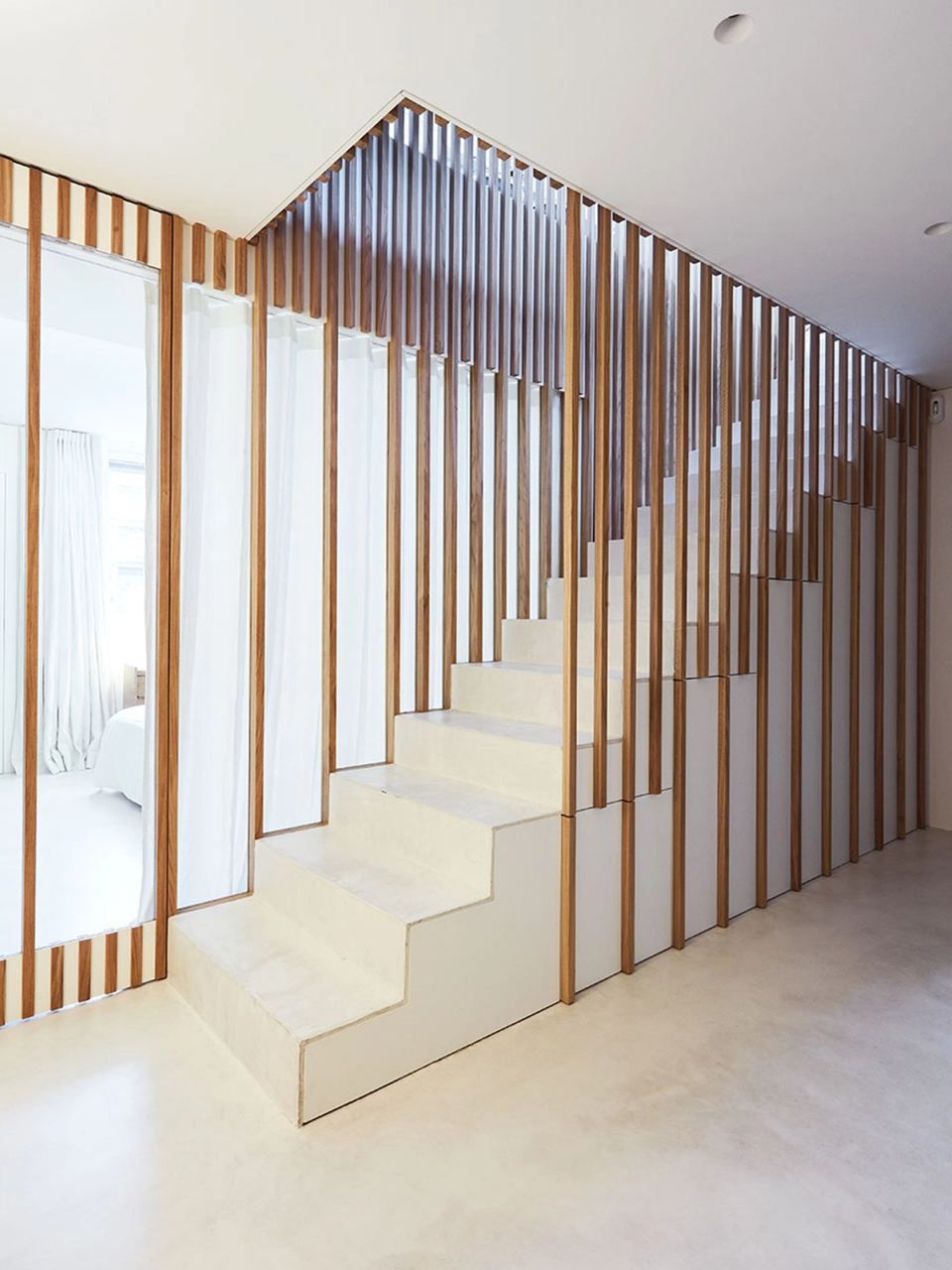 The renovation integrates bespoke architectural solutions to optimize the relationship between functionality and design. The staircase becomes a key feature thanks to a composition of vertical wooden slats that add rhythm, visual transparency and spatial continuity, reinforcing the minimalist and contemporary aesthetic of the home.