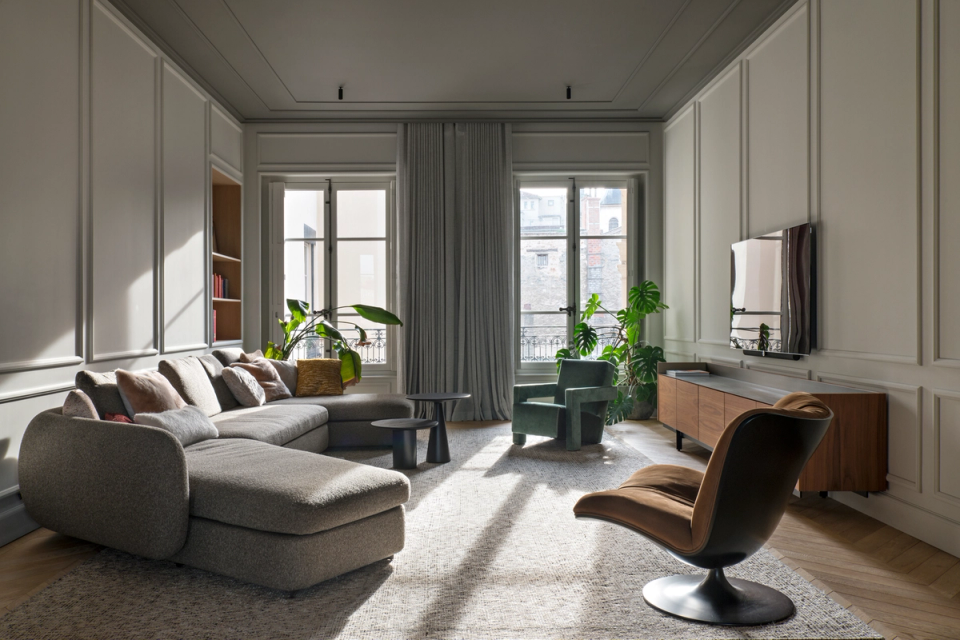 The interior renovation of this living room restores the classical elegance of the original home through ornamental moldings, large windows, and an open layout that enhances natural light. Contemporary furniture and the combination of soft textures and noble woods bring warmth and sophistication, creating a welcoming, balanced space designed for everyday comfort.