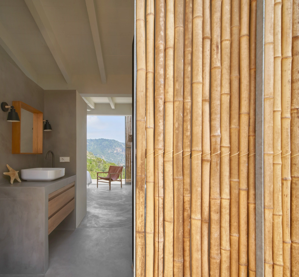 This space within the single-family home highlights the relationship between architecture, materiality, and the Mediterranean landscape. Natural cane cladding acts as a visual and solar filter, providing texture, privacy, and an organic connection with the outdoor surroundings. The combination of mineral surfaces, wooden furniture, and minimalist lines creates a warm and balanced atmosphere, while open views toward the landscape reinforce the feeling of calm and spaciousness. This single-family home stands out for contemporary architecture that prioritizes natural light, cross ventilation, and the integration of natural materials within the residential space.