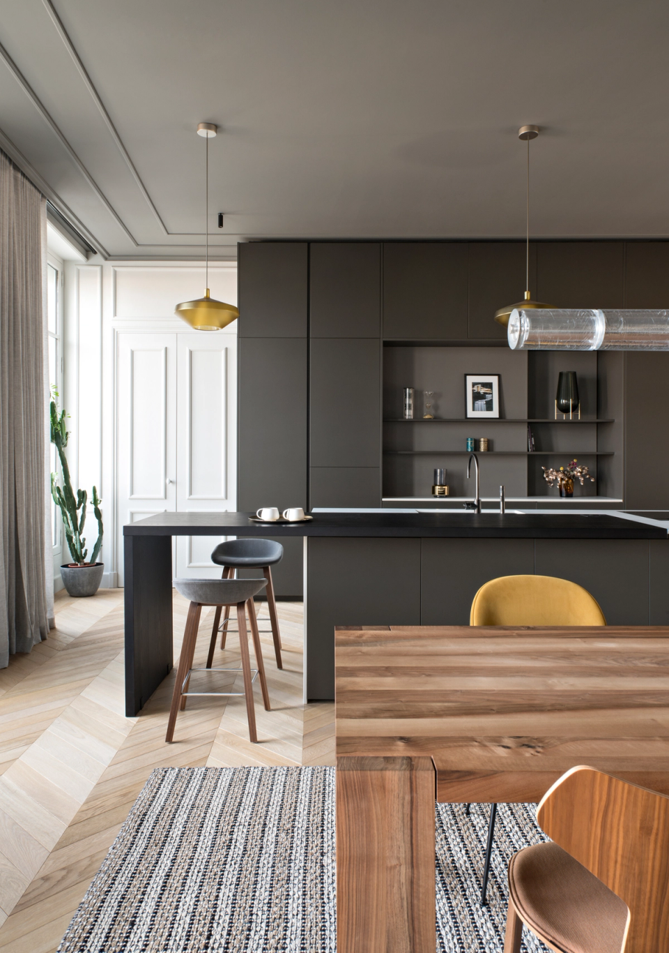 The interior renovation of this kitchen transforms the space into an elegant and functional proposal that combines the home’s classical architecture with a contemporary and minimalist design. Dark finishes, natural wood, and decorative lighting add character and sophistication, while the open layout encourages the connection between the kitchen, dining area, and living room to create a spacious, warm, and welcoming atmosphere.