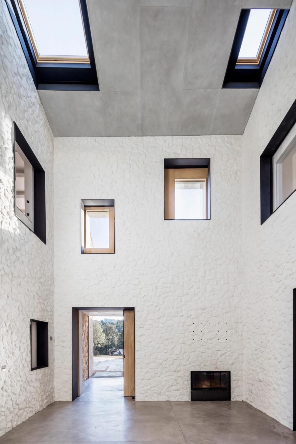 Interior zone of a full renovation featuring restored stone walls and contemporary architecture that prioritizes natural light and visual openness. Skylights integrated into the sloped ceilings allow zenithal lighting that highlights the textures of the stone and adds depth to the spaces. Geometric openings visually connect the different rooms, creating a fluid, elegant, and functional layout. This full renovation combines tradition and modernity through noble materials, minimalist finishes, and a timeless aesthetic focused on comfort and luminosity.