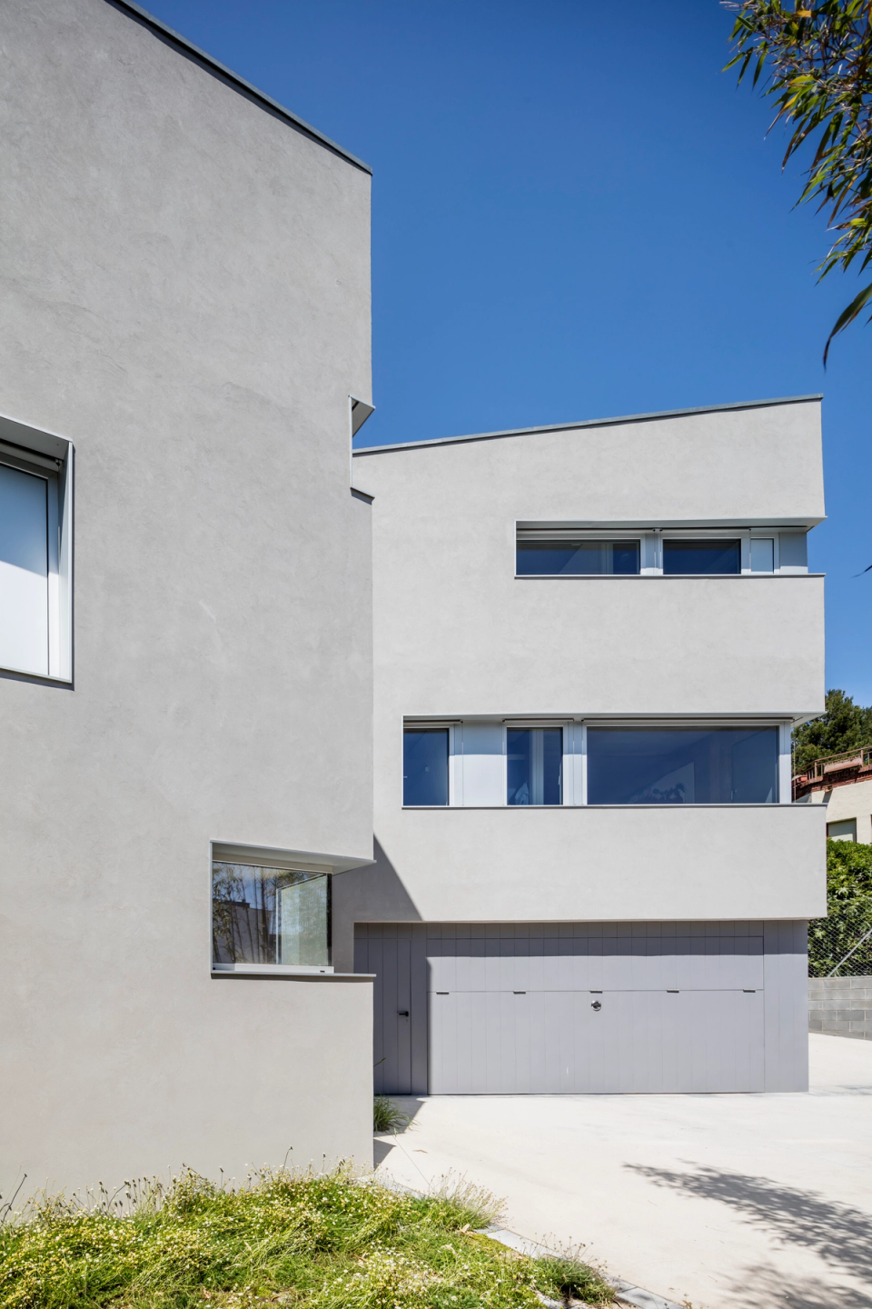 Single-family house with minimalist lines and contemporary architecture, composed of clean geometric volumes that create an elegant and functional composition. The light façades, combined with horizontal openings and large windows, enhance natural light and provide a sober and sophisticated appearance. The exterior design prioritizes formal simplicity, the integration of interior spaces, and a modern aesthetic defined by the purity of materials and architectural proportions.