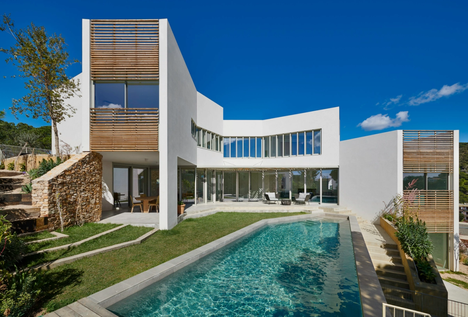 Contemporary detached single-family home with open and luminous architecture that prioritizes the relationship between interior and exterior spaces. White volumes, wooden solar protection elements, and large glazed surfaces create an elegant and functional composition integrated into the Mediterranean landscape. The swimming pool and outdoor spaces reinforce the project’s exclusive character and sense of spaciousness.