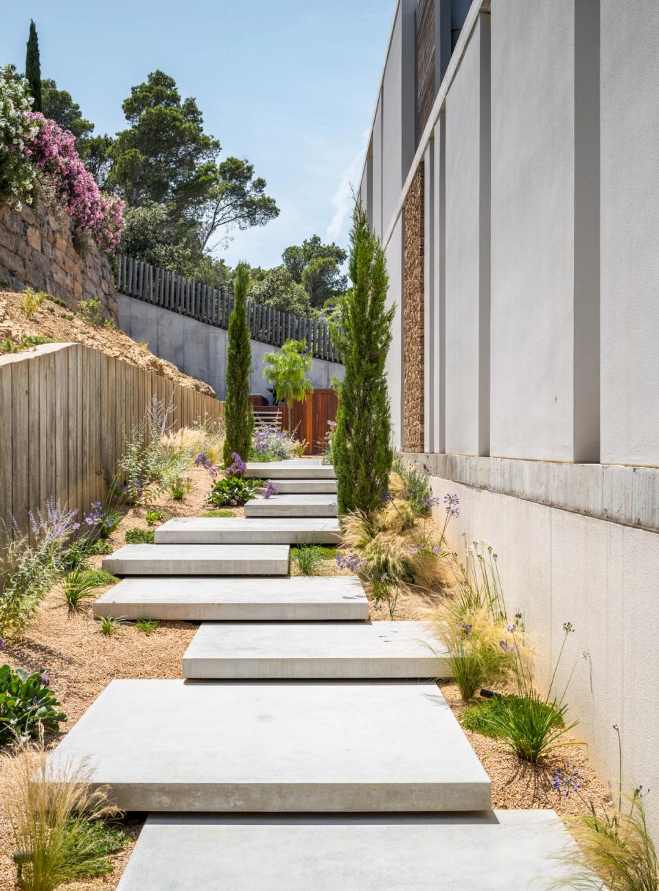 Detached single-family home with outdoor spaces designed to integrate architecture with the Mediterranean landscape. Concrete pathways, native vegetation, and natural stone finishes create an elegant, functional atmosphere connected to the environment.