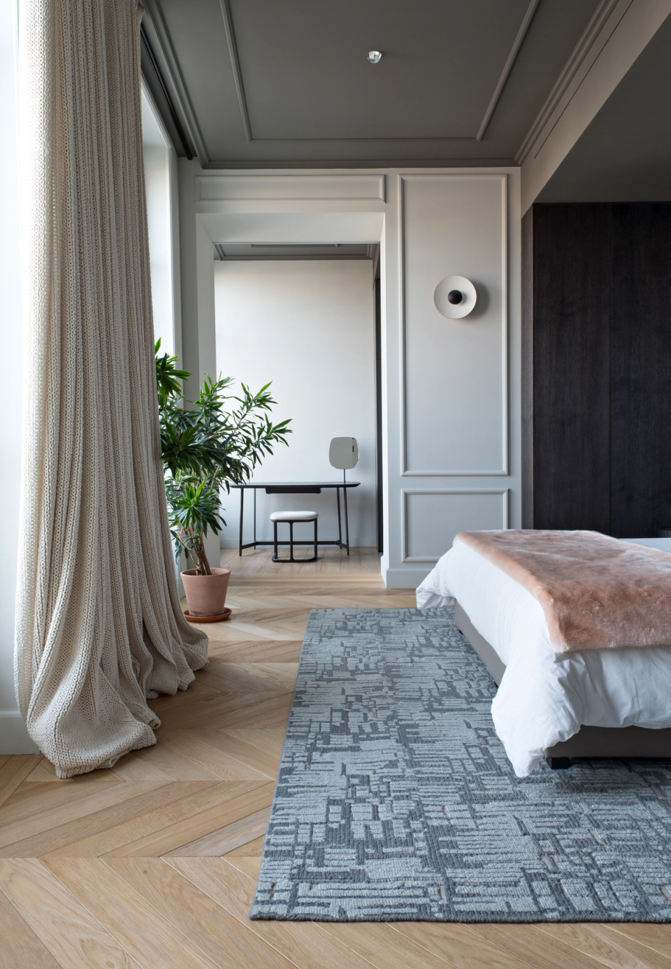 The interior renovation of this bedroom embraces a serene and sophisticated atmosphere, combining classical moldings, dark-toned ceilings, and noble materials that add depth and elegance. Natural light filtered through lightweight curtains enhances the warmth of the herringbone flooring and creates a cozy and relaxing environment. Minimalist furniture and integrated decorative details reinforce a balanced contemporary aesthetic designed to transform the space into an intimate, functional, and comfortable resting area.