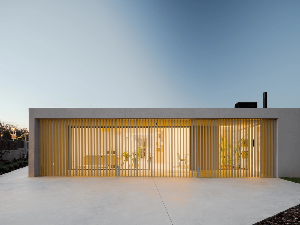 This single-family home features a light and elegant façade defined by a skin of vertical slats that filter natural light and provide privacy to the interior spaces. Transparency, warm lighting, and volumetric simplicity reinforce the contemporary character of the home, creating a balanced, subtle, and sophisticated architectural image.