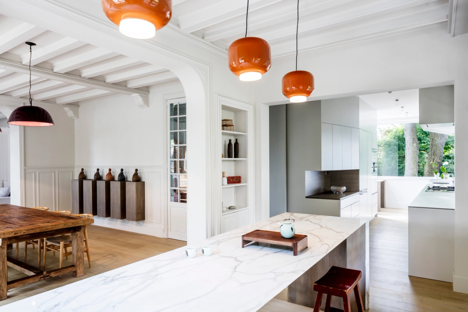 Interior renovation of an open living area connecting the kitchen, dining room, and lounge in one fluid and luminous space. The intervention preserves the original elements of the residence, such as moldings and beam ceilings, integrating them with a contemporary kitchen featuring clean lines, premium finishes, and a large marble island that becomes the center of everyday living.