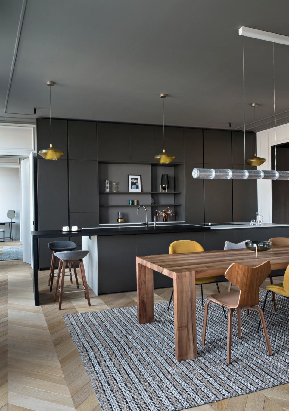he interior renovation of this kitchen-dining area redefines the space with an elegant and contemporary composition, where dark-toned furniture contrasts with the warmth of natural wood and the brightness of light finishes. The large central island and custom-made furniture enhance functionality and visual order, while the herringbone flooring and decorative lighting pieces add character and sophistication. The seamless integration between kitchen and dining area creates a spacious and welcoming environment designed for enjoying everyday life with comfort and style.