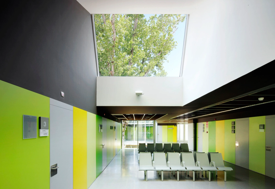 Interior waiting area of the Sant Vicenç Health Center designed to enhance comfort, natural light, and user orientation. The combination of vivid colors on the walls brings dynamism and facilitates spatial identification, while the large skylight visually connects the interior with the exterior and fills the environment with natural light.