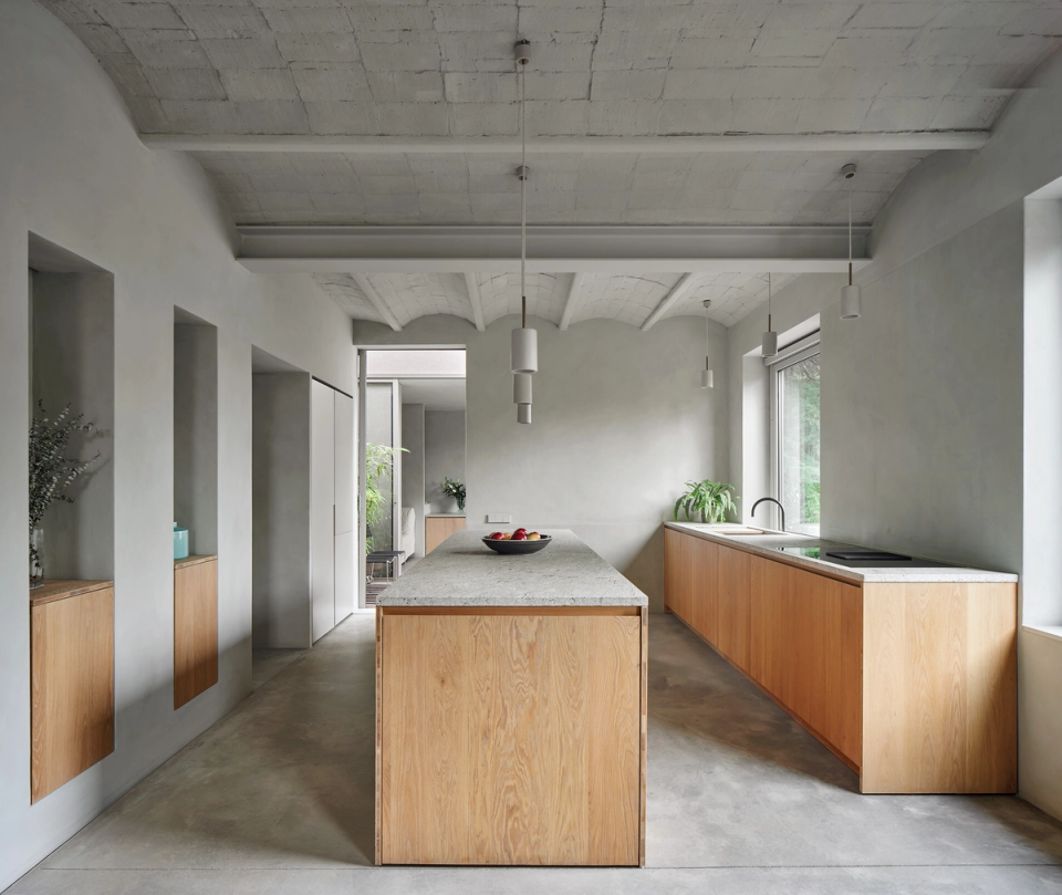 Interior of a housing renovation with an open kitchen featuring minimalist lines, natural materials and a functional layout. The wooden furniture, continuous flooring and natural light create a warm, calm and contemporary atmosphere.