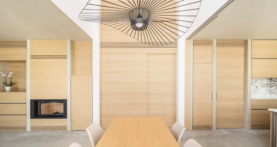 Natural wood defines and unifies the interior spaces through integrated furniture and continuous wall surfaces that provide warmth and compositional order. Natural light, double-height ceilings, and design elements reinforce the serene and contemporary atmosphere of the home.